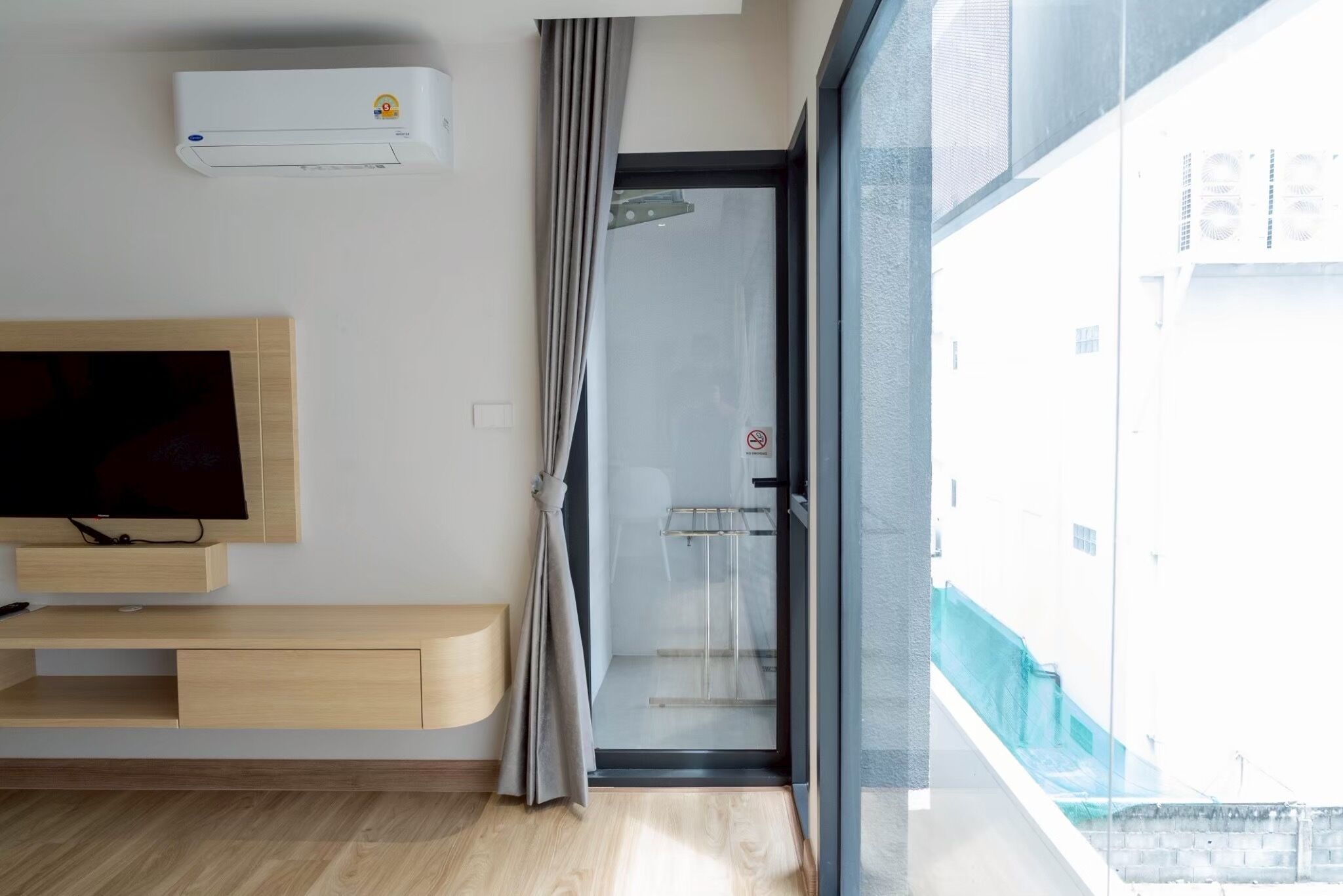 A modern room with a flat-screen TV, a wooden console, a glass shower door, and a view of the outside.