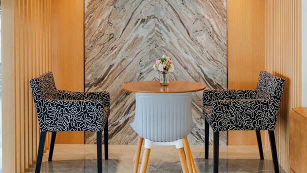 A modern dining area with a marble wall, two patterned chairs, a round table, and a vase with flowers. - I-Zen Residence Central Eastville (Bangkok)