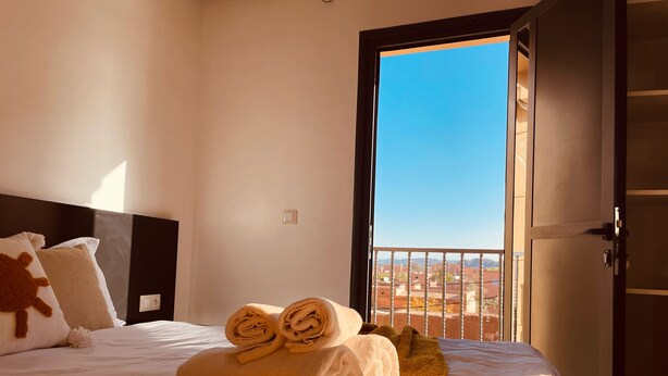 Una habitación de hotel con cama, ventana y vista a edificios, además de una puerta.