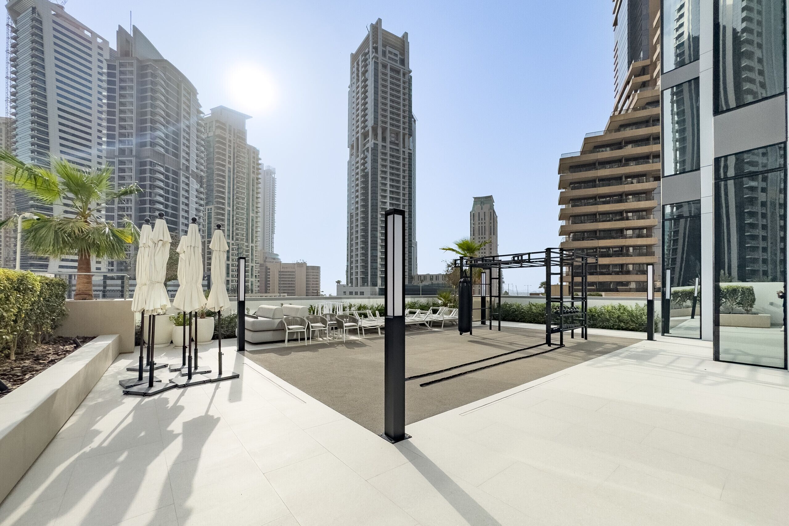 A rooftop terrace with outdoor seating, palm trees, and modern buildings in the background.