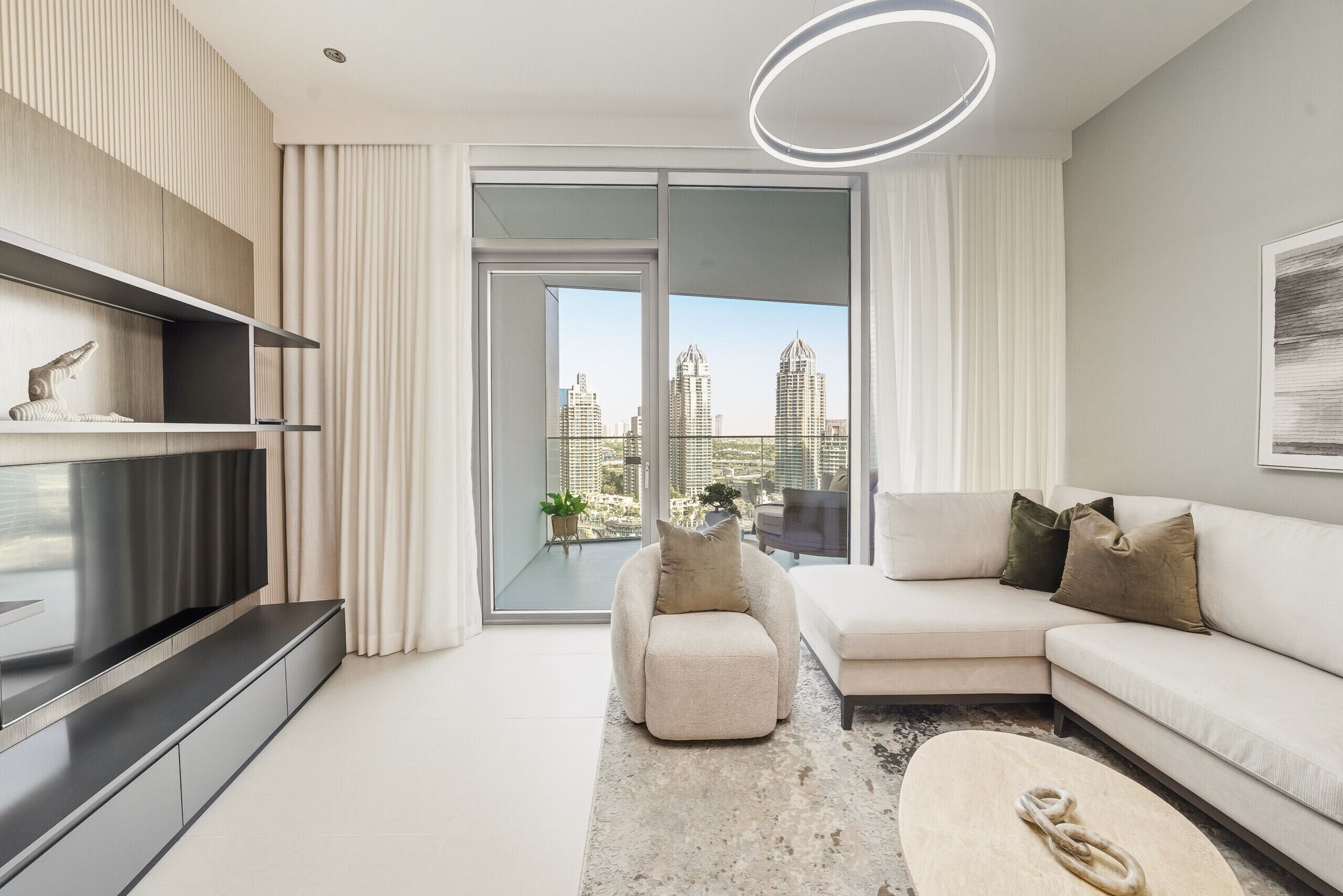 A modern living room with a flat-screen TV, a sofa, a coffee table, and a view of a cityscape through large windows.
