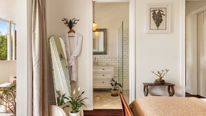 A bedroom with a bed, a bedside table, a mirror, a potted plant, and a bathroom visible through an open door. - Bruns Lifestyle - Convenient Luxury (BRUNSWICK HEADS)