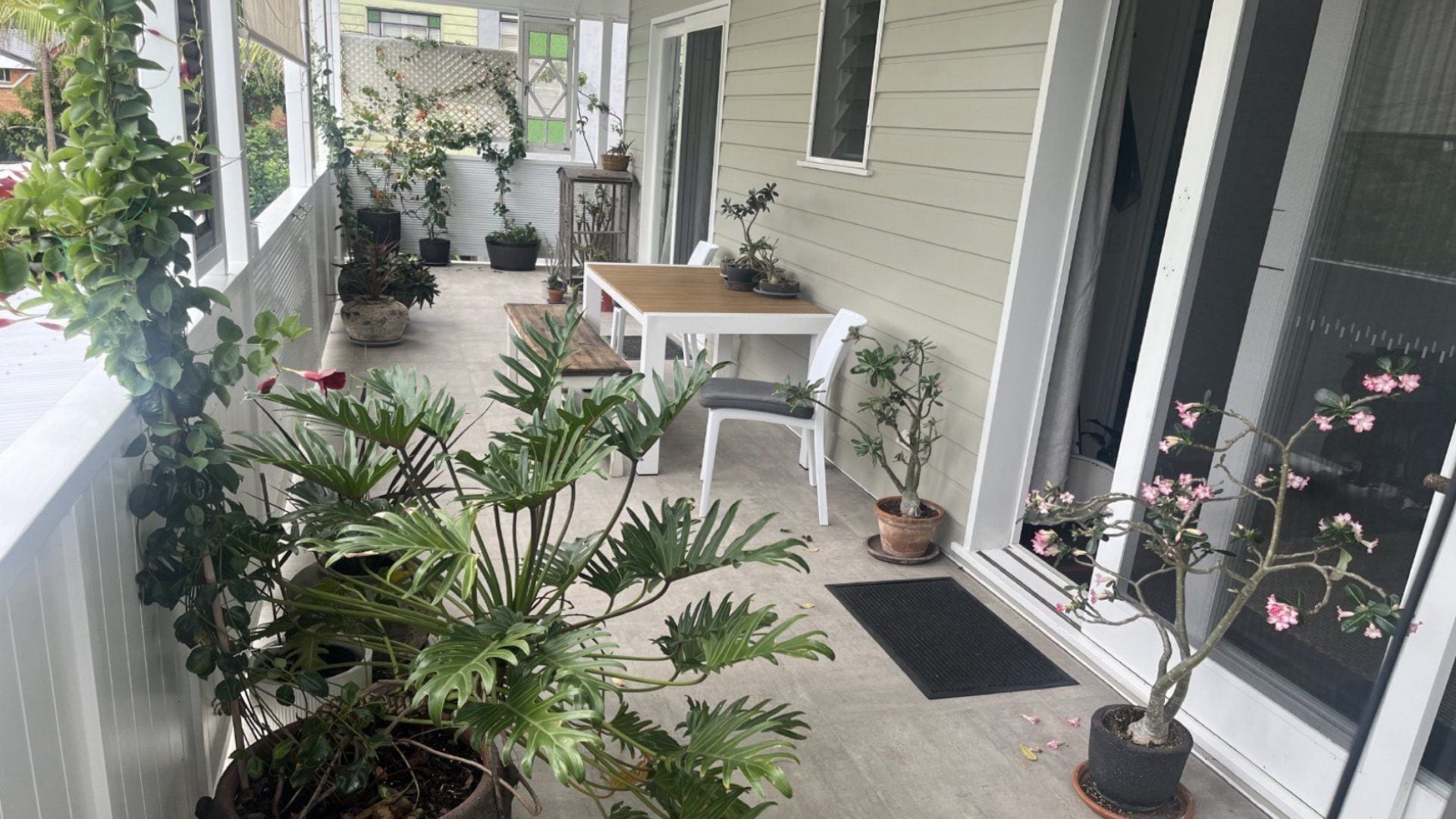 A covered porch with potted plants, a wooden table, and white chairs.