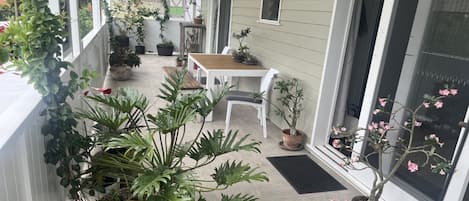 A covered porch with potted plants, a wooden table, and white chairs.