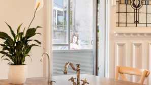 Ein Zimmer mit Blumentopf, Wasserhahn aus Metall, einem Stuhl und einem Fenster mit Blick auf ein Gebäude.