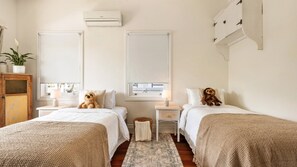 Une chambre avec deux lits, une petite table, une lampe, une plante en pot et un appareil de climatisation.