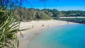 Une plage à l’eau claire, bordée d’un rivage sablonneux, avec une végétation luxuriante en arrière-plan.