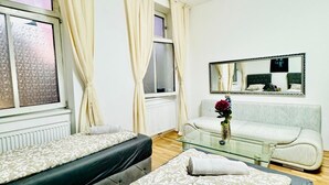 A hotel room with two beds, a sofa, a glass coffee table, a mirror, and a window with curtains. - Stylish Studio Stay Near Augarten (Vienna)