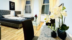 A modern living room with a sofa, a glass coffee table, and a dining area with a lace tablecloth. - Stylish Studio Stay Near Augarten (Vienna)