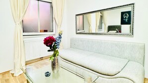 A modern living room with a glass coffee table, a light-colored sofa, a large mirror, and a window with curtains. - Stylish Studio Stay Near Augarten (Vienna)
