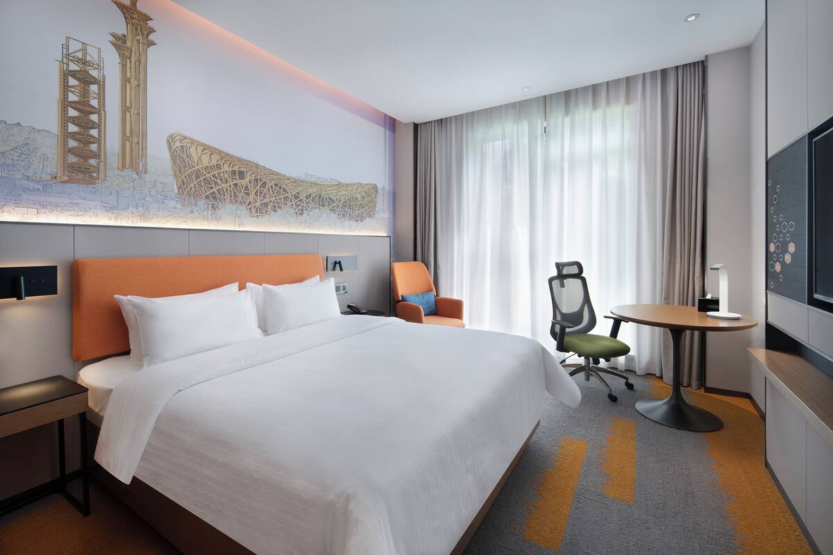 A hotel room with a large bed, a desk, a chair, a round table, and a TV.
