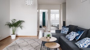 A modern living room with a grey sofa, blue patterned pillows, a potted plant, and a small round table. - Spacious 2BR City Retreat with Sauna (Helsinki)