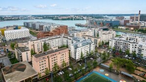 A high-rise residential building complex with multiple apartment buildings, a sports field, and a river in the background. - Spacious 2BR City Retreat with Sauna (Helsinki)