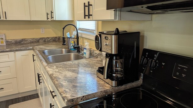 Una cocina con armarios blancos, encimera de granito, cafetera y estufa.