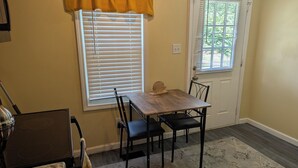 Un comedor con una mesa de madera y cuatro sillas, una ventana con persianas, una puerta y una zona de cocina con estufa.