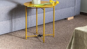 Ein graues Sofa mit einem gelben Kissen, ein kleiner runder Tisch mit einer Vase voller gelber Blumen und ein Teppichboden.