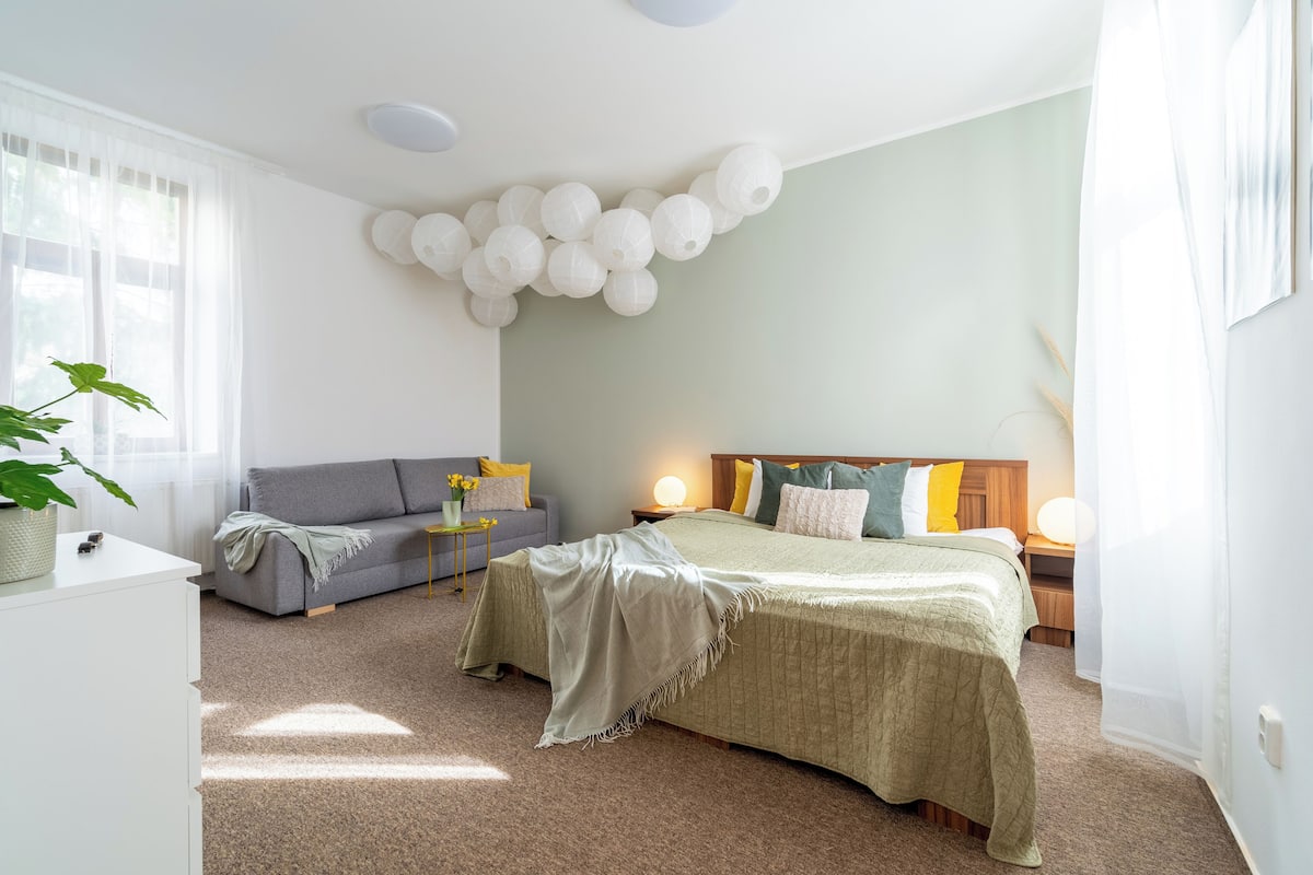 Ein Schlafzimmer mit Bett, einer Couch, einem Nachttisch, einer Lampe und einer Wanddekoration.