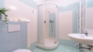 Un bagno con doccia, servizi igienici, lavandino e porta asciugamani con asciugamani.