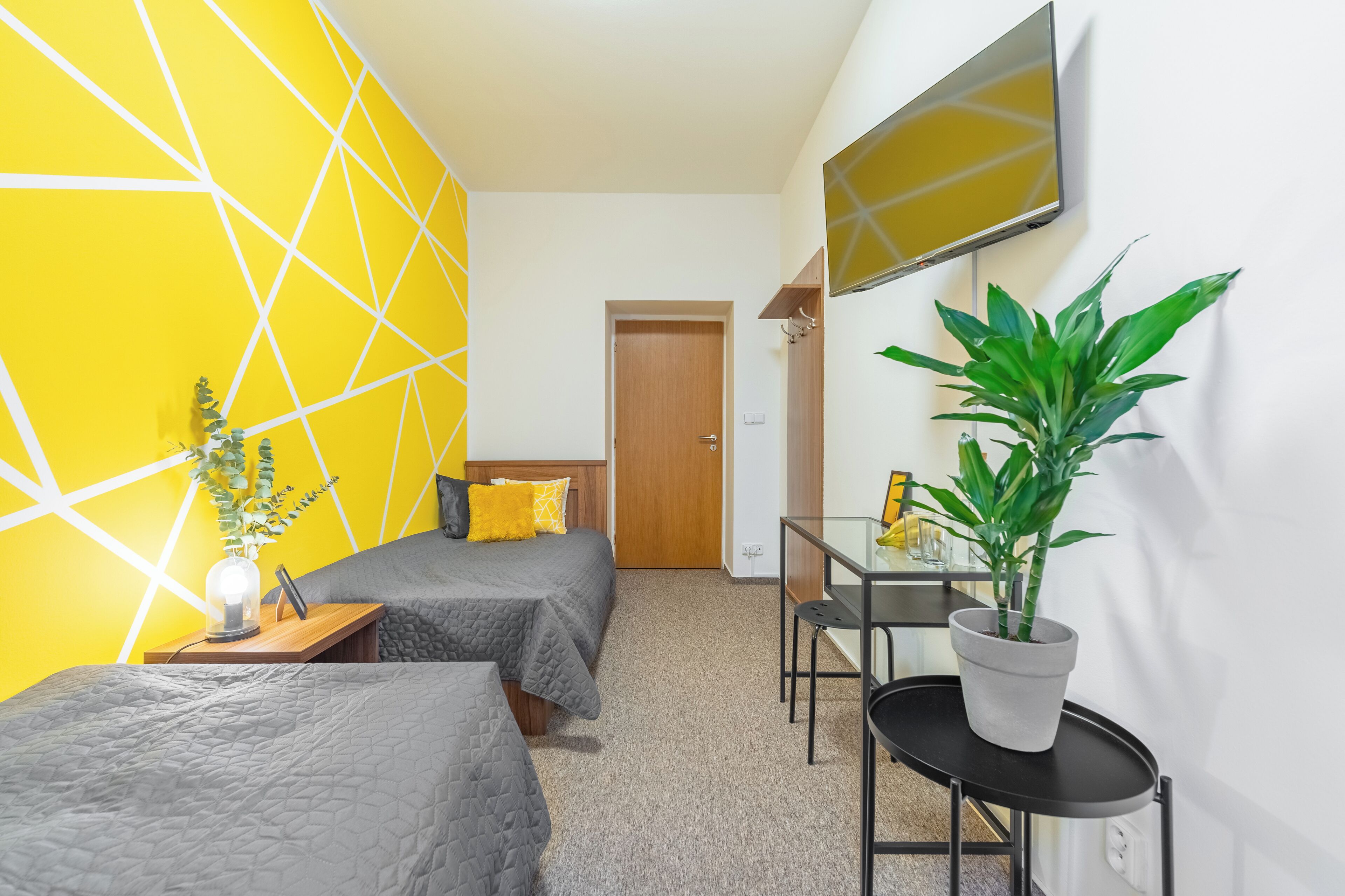 A hotel room with two beds, a desk, a chair, a TV, and a potted plant.