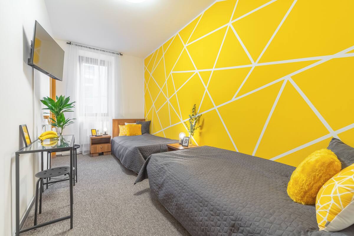 Ein Hotelzimmer mit zwei Betten, einem Fernseher, einem kleinen Tisch mit Pflanze und einem Fenster mit Vorhängen.
