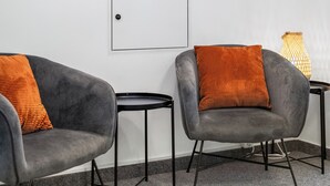 Zwei graue Sessel mit orangefarbenen Kissen, ein kleiner runder Tisch und eine weiße Tür.