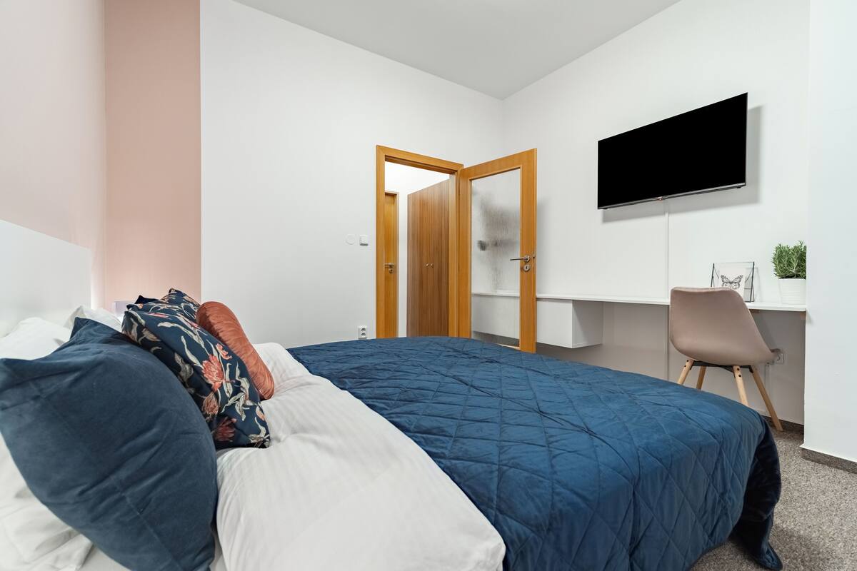 Ein Schlafzimmer mit einem Bett, einem Schreibtisch, einem Stuhl und einem Fernseher an der Wand.