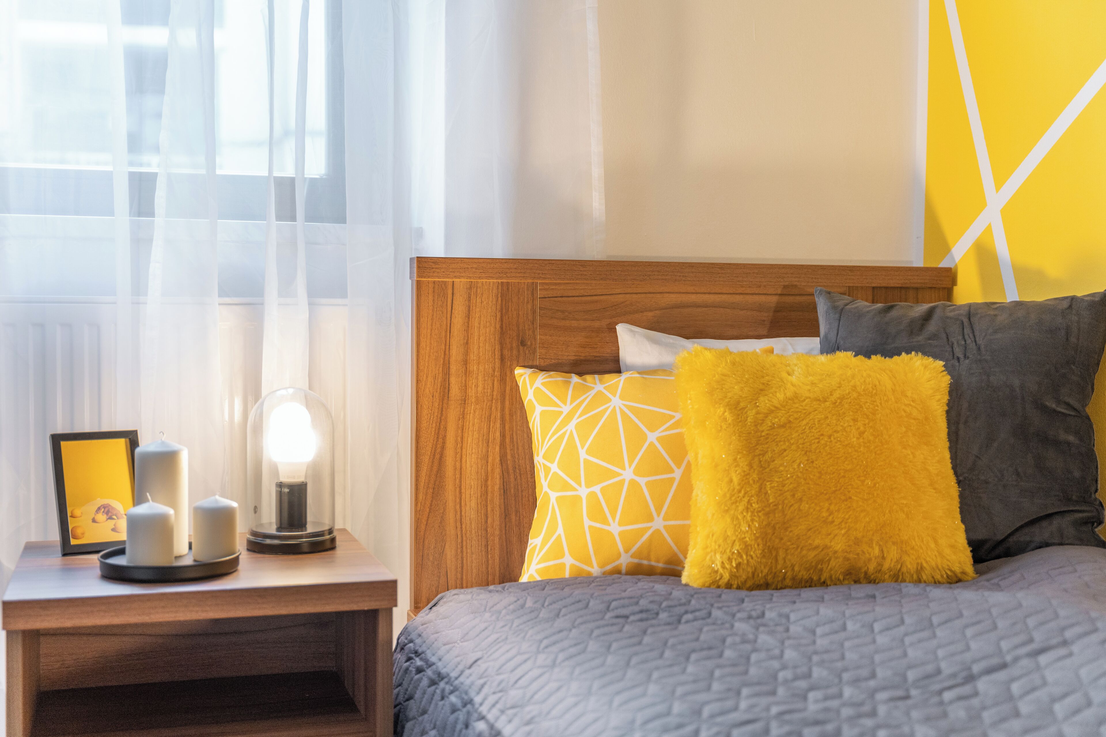 Un letto ben rifatto con una testiera in legno, un comodino con una lampada e un quadro incorniciato.