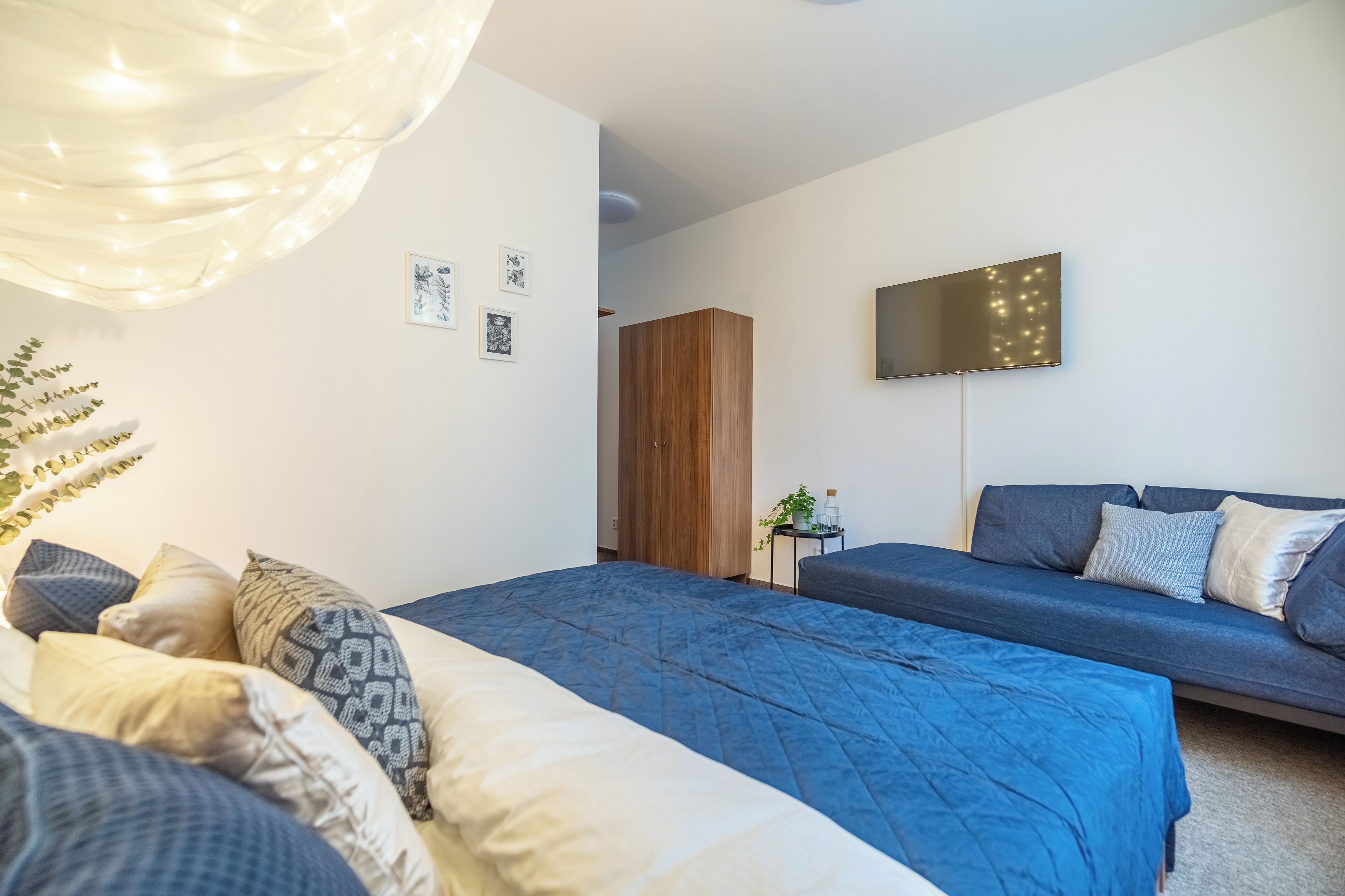 Un dormitorio moderno con una cama grande, un sofá, un televisor y un armario de madera.