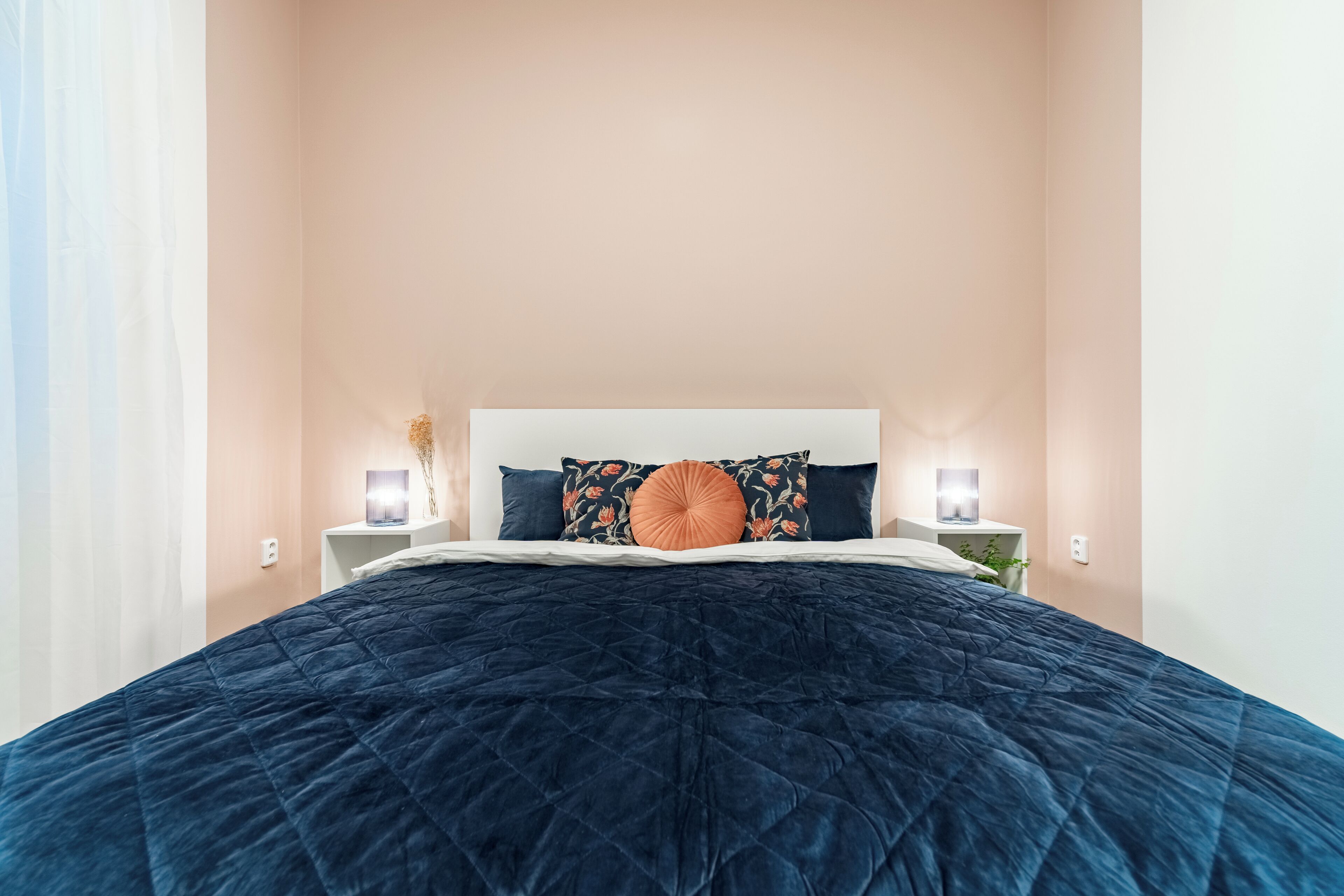 A neatly made bed with a dark blue quilt, a white headboard, and two bedside lamps on nightstands.