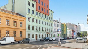 Ein mehrgeschossiges Gebäude mit einer grün-orangefarbenen Fassade, einem sichtbaren 'Expolo Living'-Schild und einem Parkschild, das einen nahegelegenen Parkplatz anzeigt.