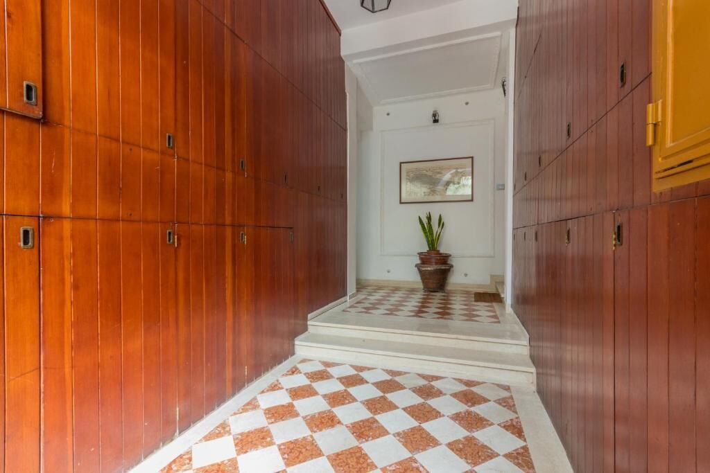 A hallway with wooden paneling and a checkered floor, leading to a room with a potted plant and a framed picture on the wall.