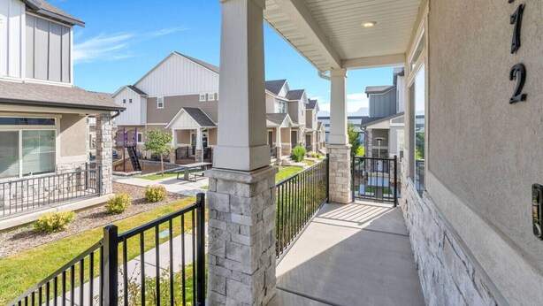 A residential building with a covered porch, stone pillars, and a view of neighboring houses. - Comfort Stay w/ Studio • Thanksgiving Point (Lehi)