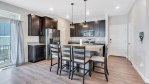 A modern kitchen with dark cabinetry, a central island, and pendant lighting. - Comfort Stay w/ Studio • Thanksgiving Point (Lehi)