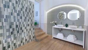 Un baño moderno con cabina de ducha azulejada, un lavamanos con dos espejos y un estante con toallas.