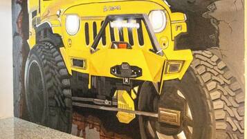 Une fresque représentant un véhicule tout-terrain jaune sur un mur dont le motif imite un mur de briques.