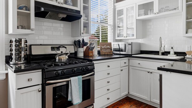 Una cocina con muebles blancos, una estufa y un lavaplatos.