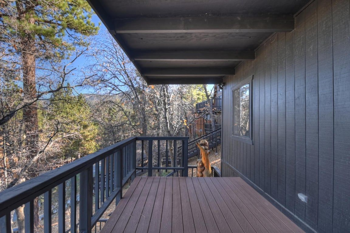 A wooden deck with a railing, overlooking a forested area.