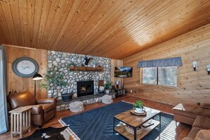 Ein gemütliches Blockhaus-Interieur mit Kamin aus Stein, Ledersofas, einem Couchtisch und einem an der Wand befestigten Fernseher.