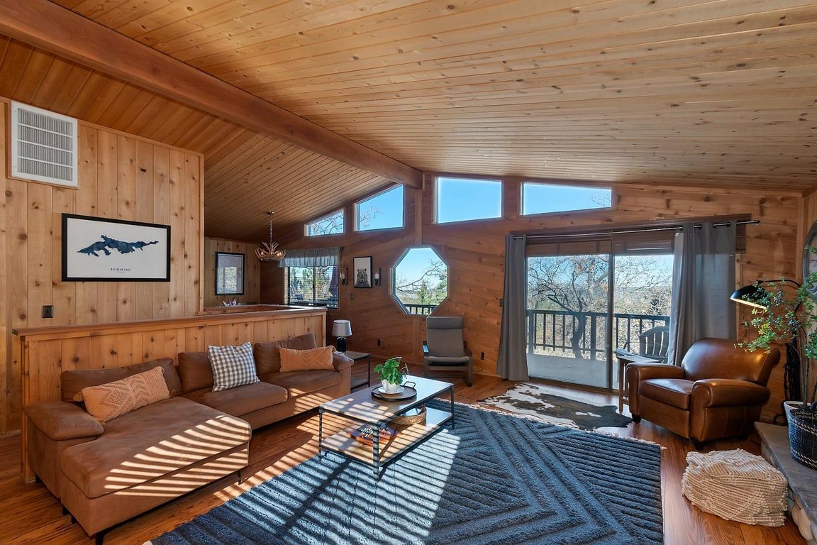 Ein Holzblockbau-Innenraum mit einer Couch, Sesseln, einem Couchtisch und einem großen Fenster.