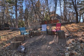 A forested area with a dirt path, wooden stumps, and three chairs. - Close to Bear Mountain Ski Resort, Golf Course and Zoo! PET FRIENDLY 🐾! Rock Fireplace! Mountain Views! (Big Bear City)