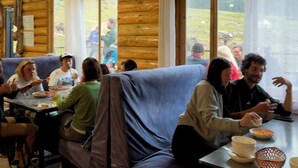 A cozy cabin-style dining area with wooden walls, large windows, and a mix of seating options including a couch and tables. - Arashan Hotel (Teploklyuchenka)