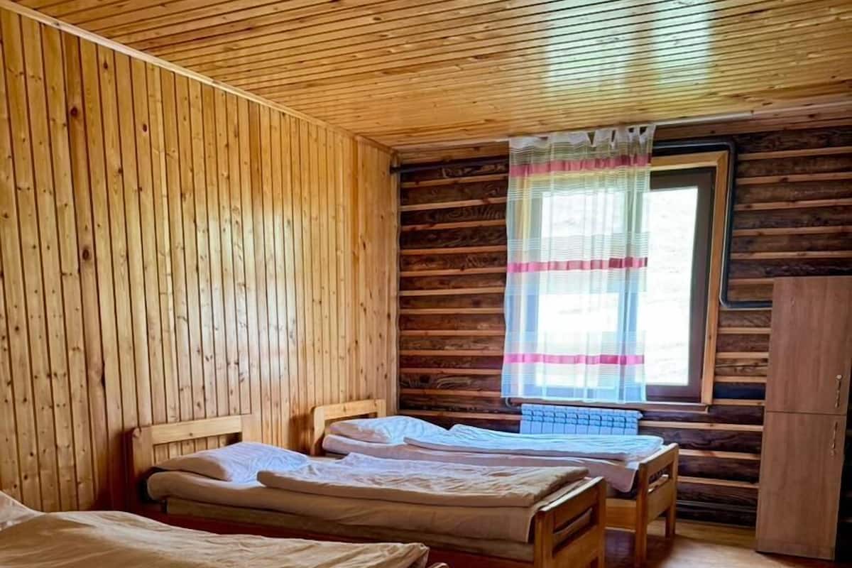 A cabin with three wooden beds, a window with curtains, and a wooden wardrobe.