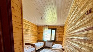 A cabin with wooden walls and floors, two single beds, a window, and a door. - Arashan Hotel (Teploklyuchenka)
