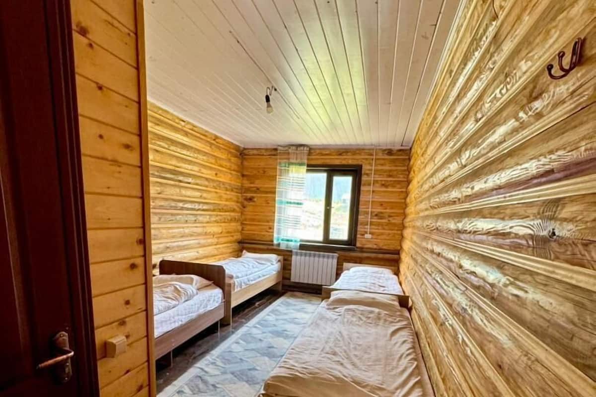 A cabin with wooden walls and floors, two single beds, a window, and a door.
