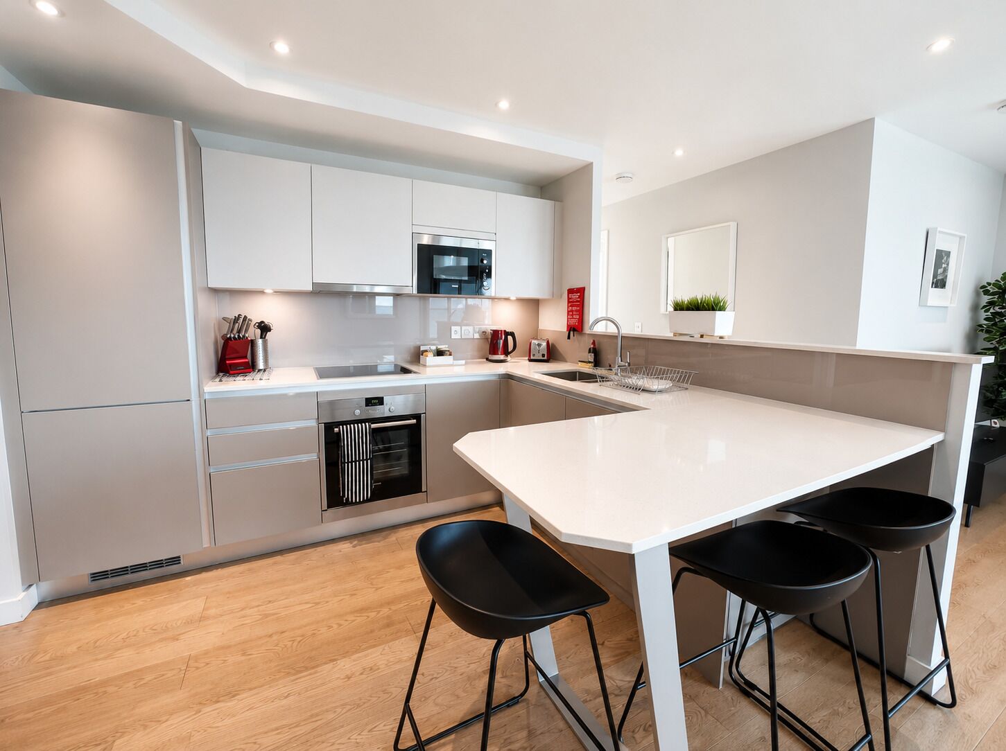 A modern kitchen with a white countertop, stainless steel appliances, and black bar stools.