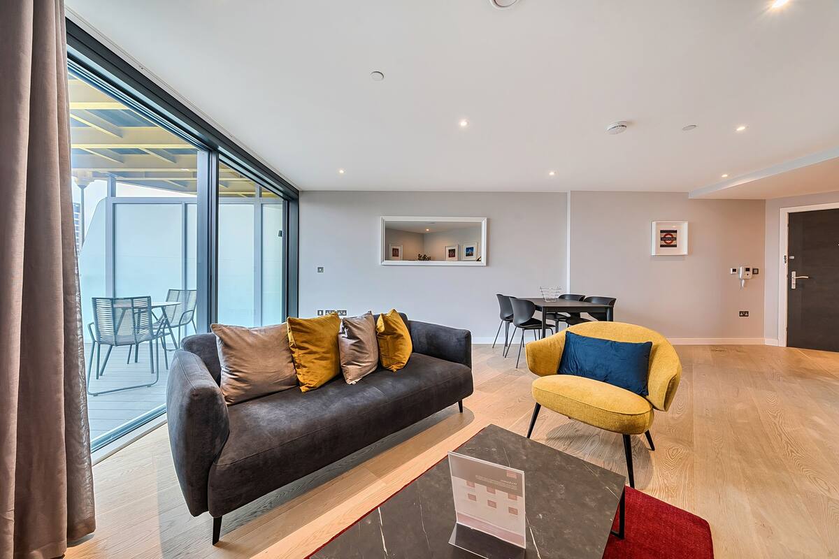 A modern living room with a dark sofa, yellow armchair, and a dining area with a table and chairs.