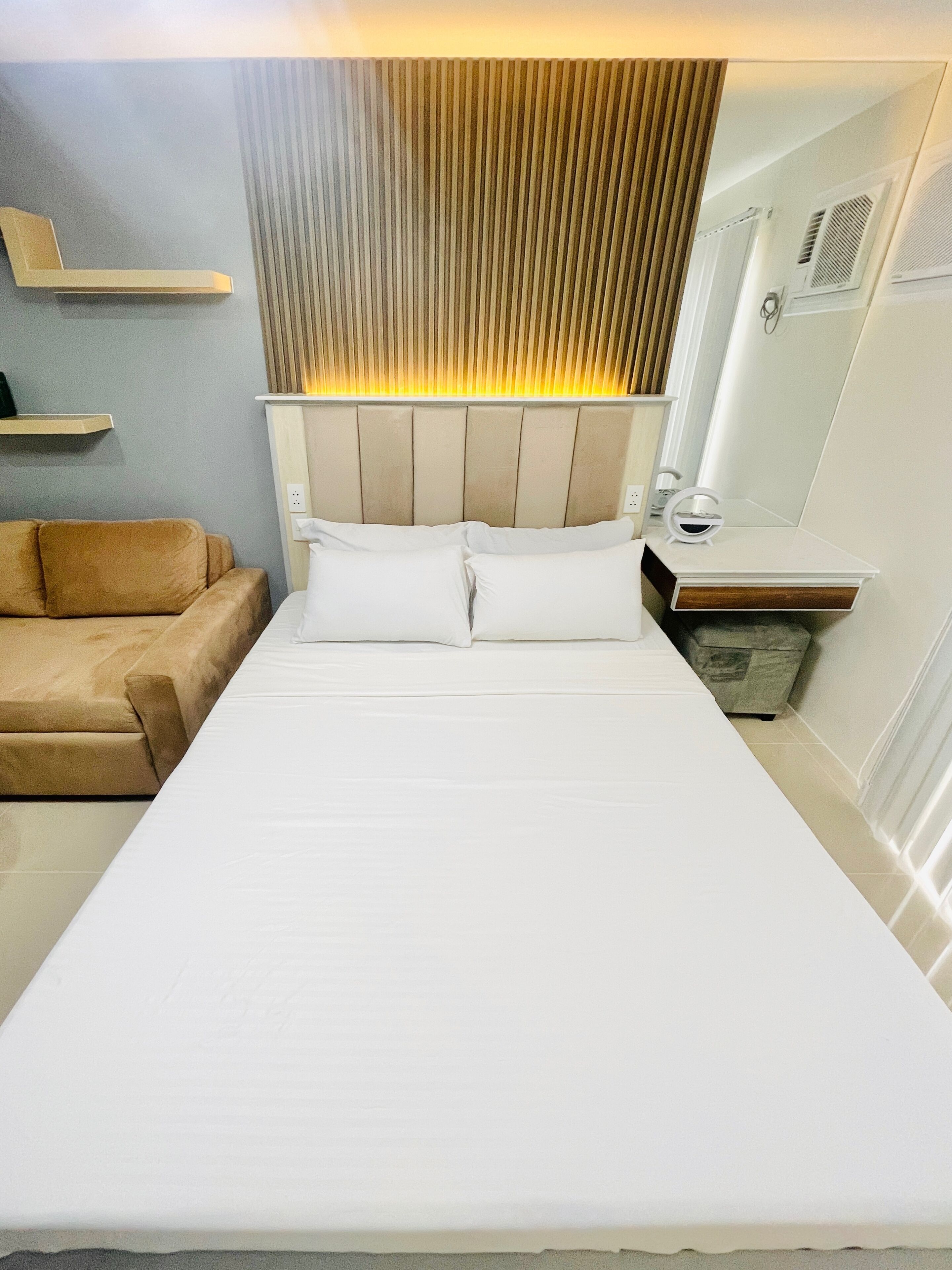 Ein Hotelzimmer mit einem Bett, einem Nachttisch, einem Spiegel, einer kleinen Ablagefläche und einem braunen Sofa.