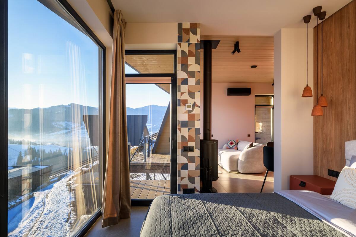Une chambre d’hôtel moderne dotée d’une grande fenêtre, d’un lit, d’un canapé et d’une cheminée.