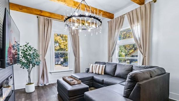 A modern living room with a sectional sofa, a chandelier, and a large window with curtains. - 6BR Gem in Midtown Atlanta (Atlanta)