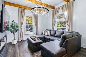 A modern living room with a sectional sofa, a chandelier, and a large window with curtains. - 6BR Gem in Midtown Atlanta (Atlanta)